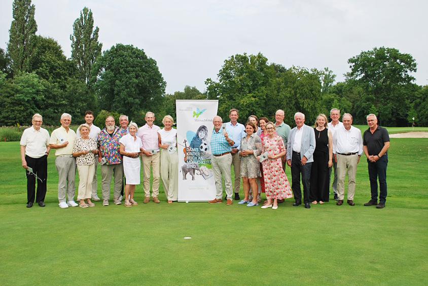 Gruppe von Personen posiert auf einem Golfplatz vor einem Banner mit der Aufschrift „Damit Kinder reichen Möglichkeiten sind“.